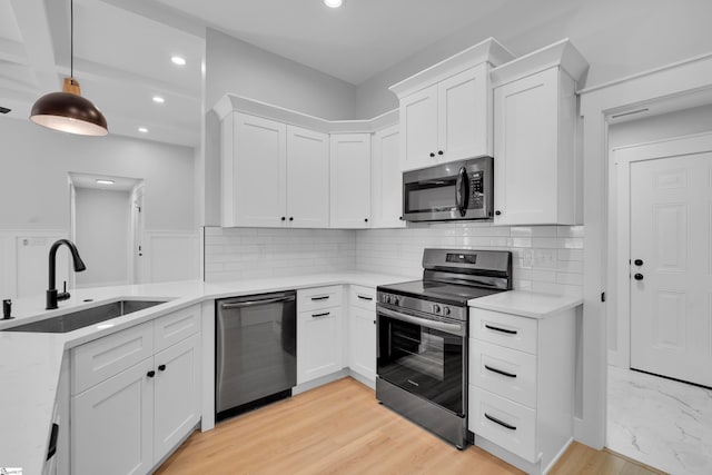 kitchen with light wood-type flooring, decorative light fixtures, sink, appliances with stainless steel finishes, and white cabinets