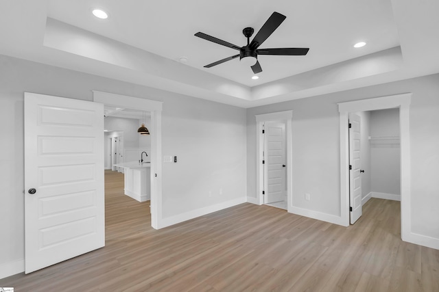 unfurnished bedroom with light hardwood / wood-style flooring, sink, a closet, a tray ceiling, and ceiling fan