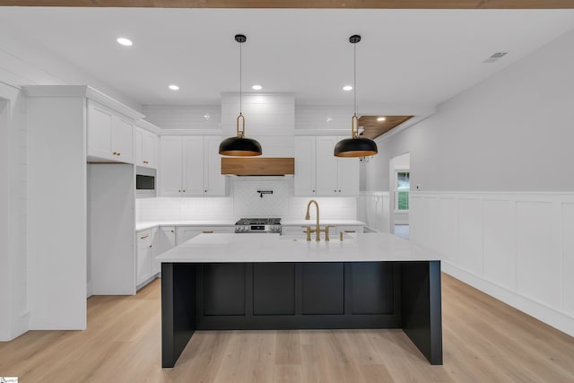 kitchen with white cabinets, hanging light fixtures, a kitchen island with sink, and light hardwood / wood-style flooring