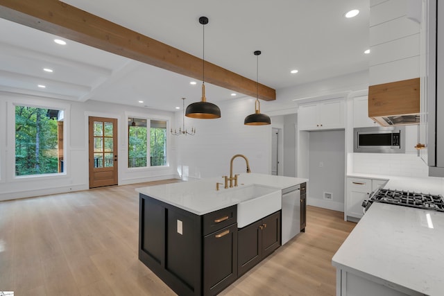 kitchen with a center island with sink, stainless steel appliances, light stone counters, and beam ceiling