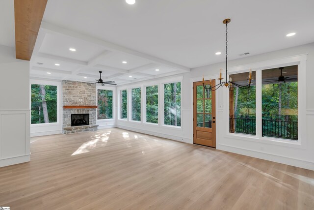 unfurnished living room with coffered ceiling, ceiling fan with notable chandelier, light hardwood / wood-style floors, and a stone fireplace