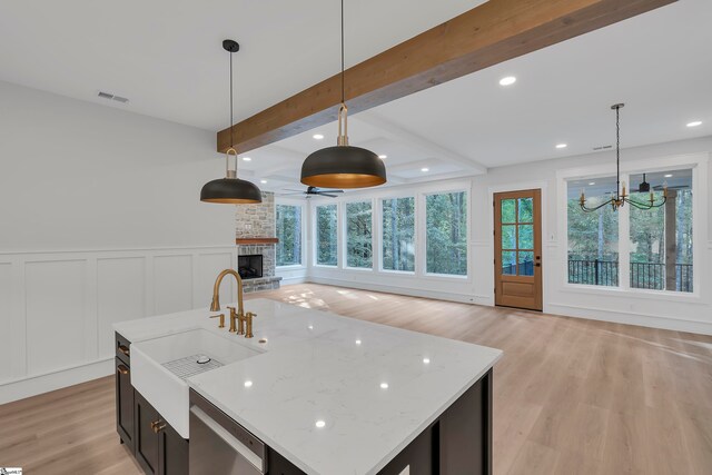 kitchen with light wood-type flooring, a fireplace, a center island with sink, and sink