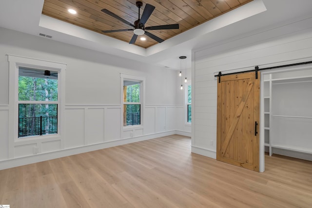 unfurnished bedroom featuring a barn door, a raised ceiling, wooden ceiling, and light hardwood / wood-style flooring