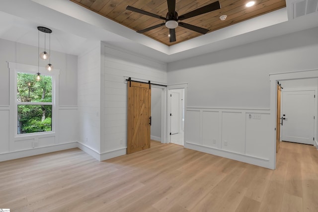 spare room with a tray ceiling, light hardwood / wood-style floors, wood ceiling, a barn door, and ceiling fan