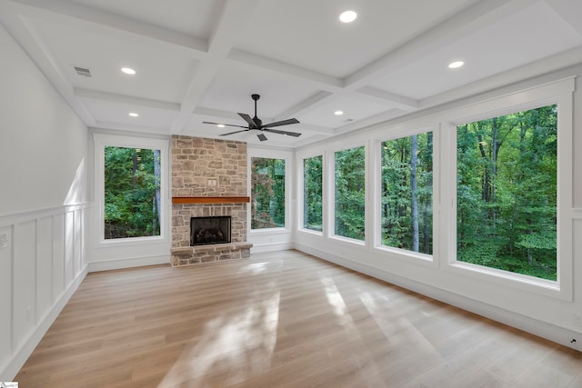 unfurnished living room featuring a wealth of natural light, ceiling fan, a stone fireplace, and light hardwood / wood-style floors