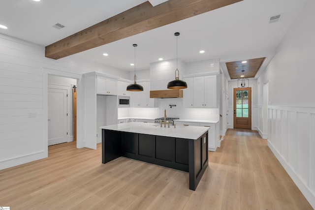 kitchen with beamed ceiling, decorative light fixtures, light hardwood / wood-style floors, a kitchen island with sink, and white cabinetry