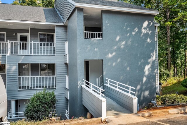 exterior space with stairs, roof with shingles, and stucco siding