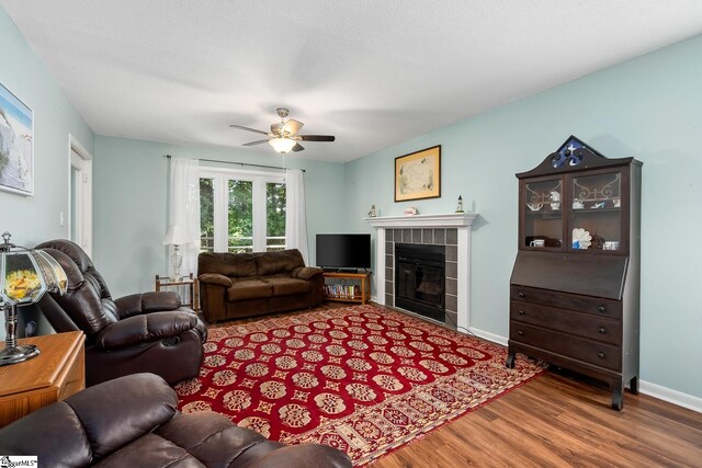 living area featuring ceiling fan, a textured ceiling, a fireplace, wood finished floors, and baseboards