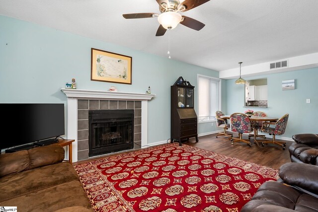 living room featuring a tile fireplace, visible vents, baseboards, and wood finished floors