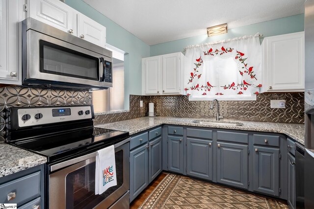 kitchen with appliances with stainless steel finishes, light stone counters, a sink, white cabinetry, and backsplash