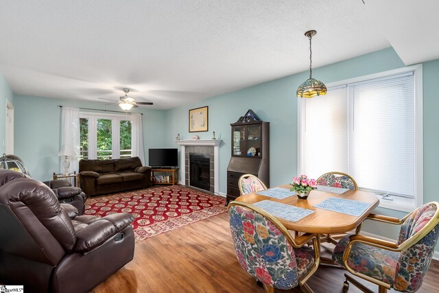 living area with a ceiling fan, a fireplace, a textured ceiling, and wood finished floors