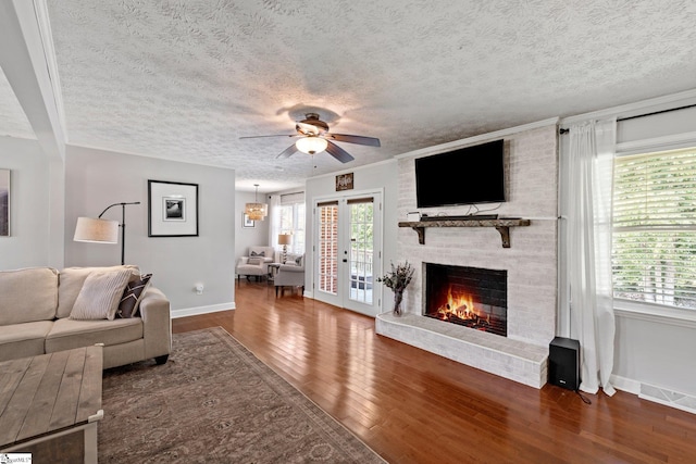 living room with dark wood-type flooring, ceiling fan, a textured ceiling, and a brick fireplace