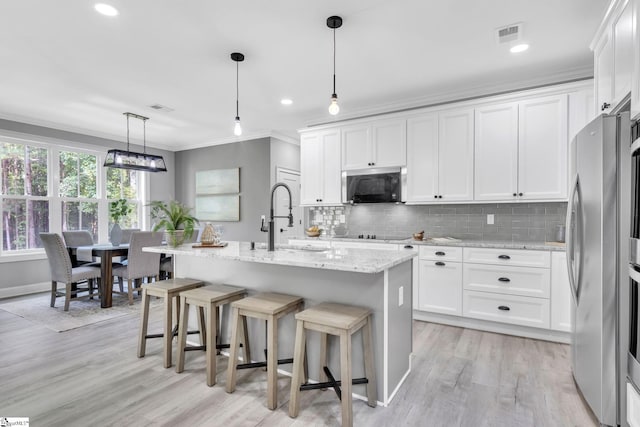 kitchen featuring hanging light fixtures, stainless steel appliances, light hardwood / wood-style floors, sink, and a center island with sink