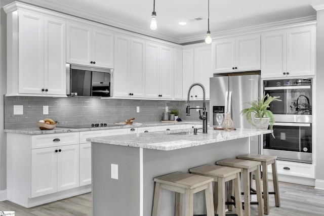 kitchen with white cabinets, hanging light fixtures, stainless steel appliances, and light hardwood / wood-style floors