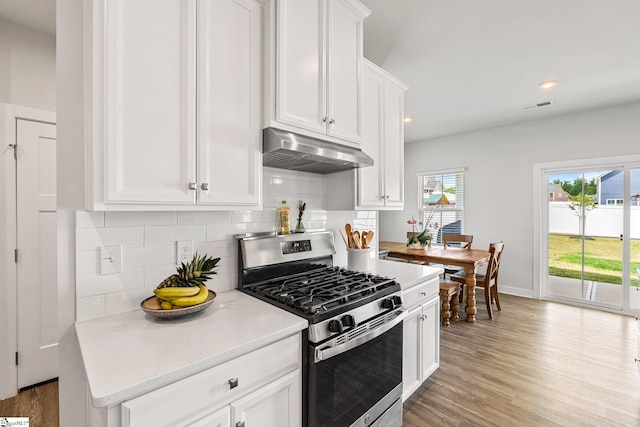 kitchen with white cabinets, decorative backsplash, light wood-type flooring, light stone countertops, and stainless steel range with gas cooktop