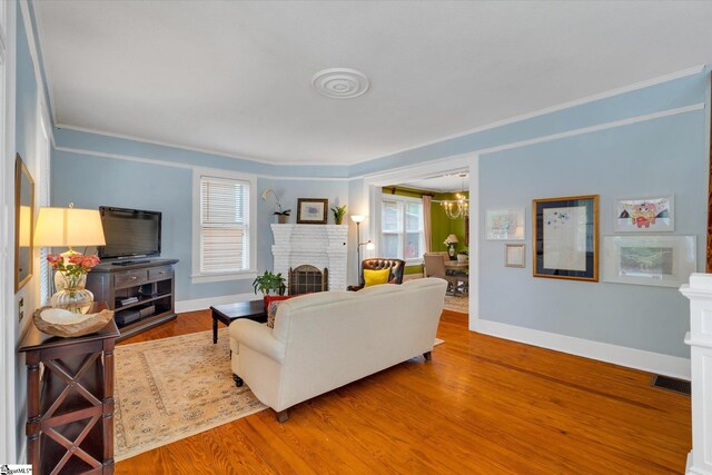 living room with wood-type flooring, ornamental molding, a notable chandelier, and a brick fireplace