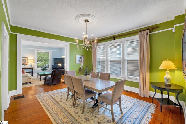 dining space with a textured ceiling, wood-type flooring, and an inviting chandelier