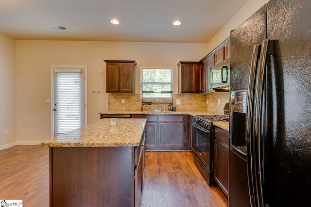 kitchen featuring light hardwood / wood-style flooring, black appliances, a kitchen island, sink, and light stone countertops