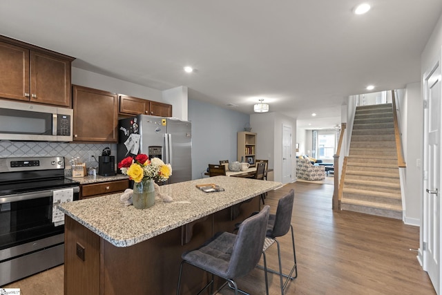 kitchen featuring light wood-type flooring, stainless steel appliances, light stone counters, a kitchen island, and a breakfast bar area