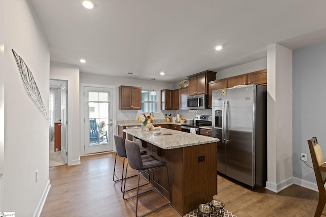 kitchen with hanging light fixtures, a kitchen island, stainless steel appliances, and light hardwood / wood-style flooring