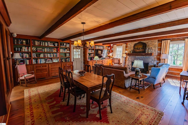 dining room featuring a notable chandelier, beam ceiling, a stone fireplace, and wood-type flooring