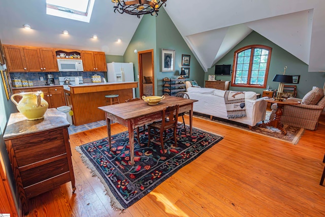 dining area featuring vaulted ceiling with skylight, light hardwood / wood-style floors, and an inviting chandelier