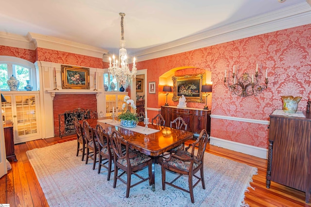 dining space with a fireplace, an inviting chandelier, light wood-type flooring, and crown molding