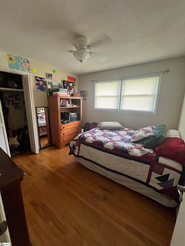 bedroom with hardwood / wood-style floors, ceiling fan, a closet, and a textured ceiling