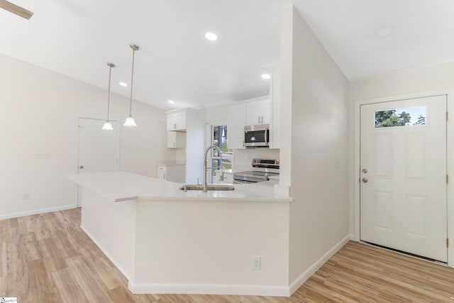 kitchen with decorative light fixtures, stainless steel appliances, kitchen peninsula, sink, and light hardwood / wood-style floors