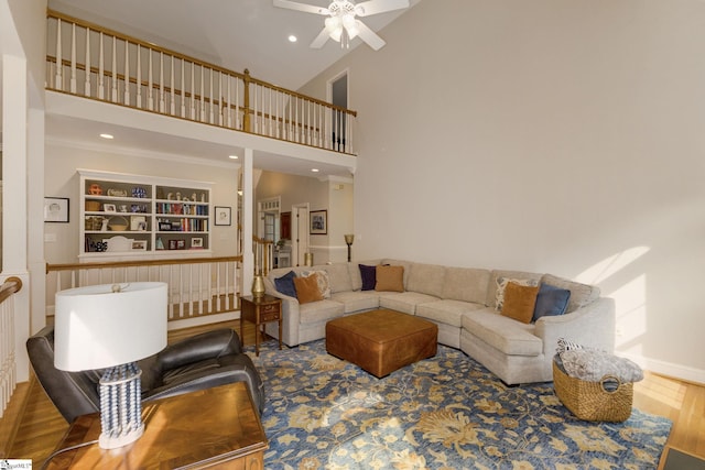 living room featuring a high ceiling, wood-type flooring, built in shelves, crown molding, and ceiling fan