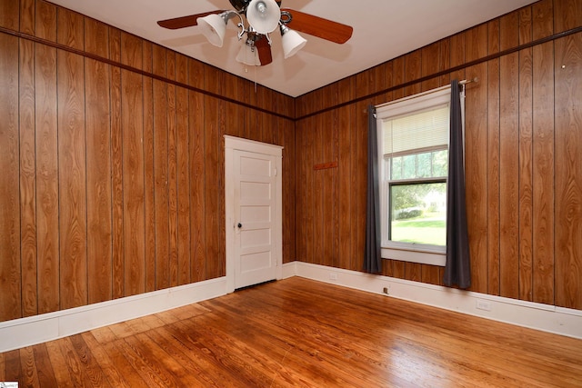 empty room with hardwood / wood-style floors, ceiling fan, and wood walls