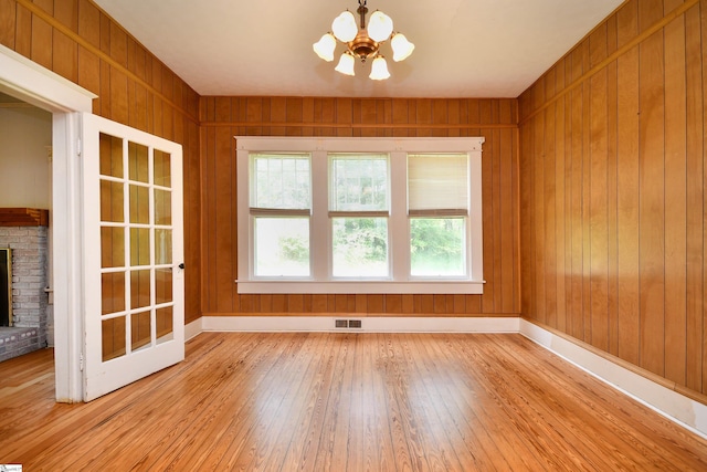 unfurnished room featuring light wood-type flooring, a brick fireplace, an inviting chandelier, and wooden walls