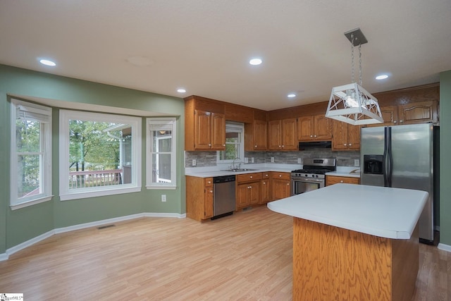 kitchen with hanging light fixtures, stainless steel appliances, sink, and light hardwood / wood-style flooring