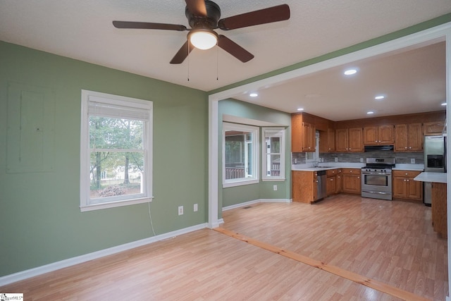 kitchen with light wood-type flooring, sink, ceiling fan, decorative backsplash, and appliances with stainless steel finishes