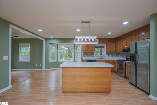 kitchen with hanging light fixtures, a center island, light wood-type flooring, stainless steel appliances, and sink