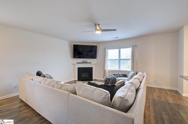 living area featuring ceiling fan, visible vents, baseboards, a glass covered fireplace, and dark wood-type flooring