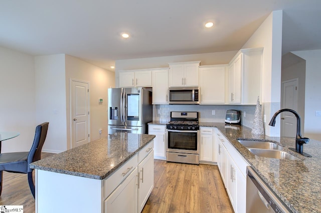 kitchen featuring dark stone countertops, white cabinetry, a sink, light wood-style flooring, and appliances with stainless steel finishes
