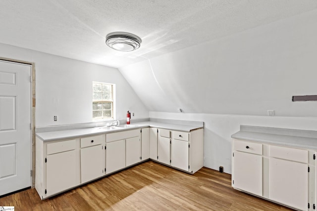 kitchen featuring light hardwood / wood-style flooring, vaulted ceiling, and white cabinetry