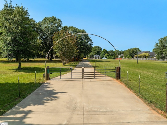 view of home's community with a lawn, a gate, fence, and concrete driveway