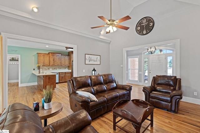 living room featuring light wood-type flooring, ceiling fan with notable chandelier, crown molding, and vaulted ceiling