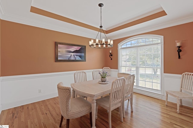 dining room featuring ornamental molding, light wood-style floors, a tray ceiling, an inviting chandelier, and wainscoting