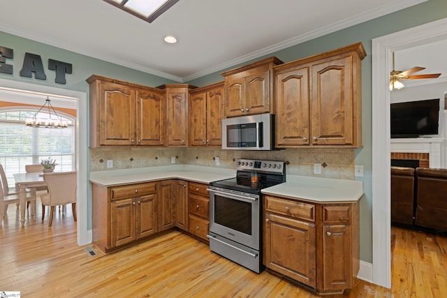 kitchen with stainless steel appliances, ceiling fan with notable chandelier, light wood-type flooring, and a fireplace