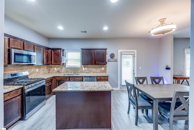 kitchen featuring light stone countertops, light hardwood / wood-style flooring, backsplash, appliances with stainless steel finishes, and a center island