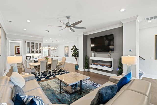 living room featuring ceiling fan with notable chandelier, dark hardwood / wood-style floors, and crown molding