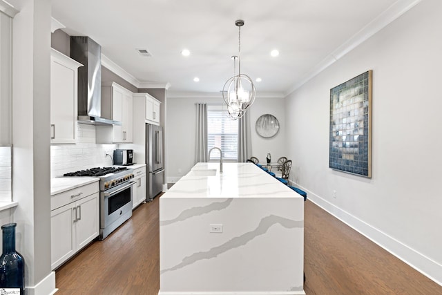 kitchen with hanging light fixtures, stainless steel appliances, wall chimney range hood, an island with sink, and dark wood-type flooring