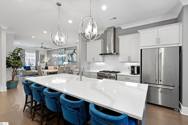 kitchen with ceiling fan with notable chandelier, dark hardwood / wood-style flooring, stainless steel appliances, white cabinetry, and wall chimney range hood