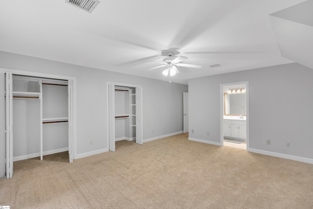 unfurnished bedroom with ensuite bath, ceiling fan, multiple closets, vaulted ceiling, and light carpet