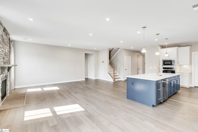 kitchen featuring white cabinetry, light hardwood / wood-style flooring, a stone fireplace, blue cabinets, and appliances with stainless steel finishes