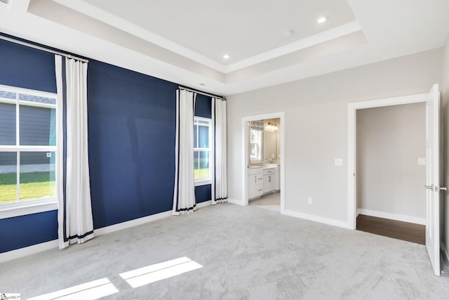 unfurnished bedroom featuring ensuite bath, a raised ceiling, and light colored carpet