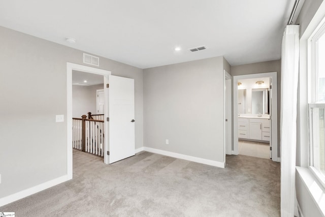 unfurnished bedroom with ensuite bath, light carpet, and multiple windows